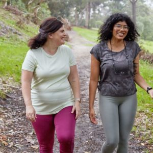 Two women walk through the forest discussing mental health adult services.