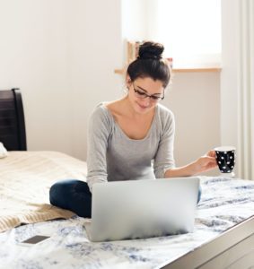 a woman sitting at her laptop drinking coffee and reading the wellness blog